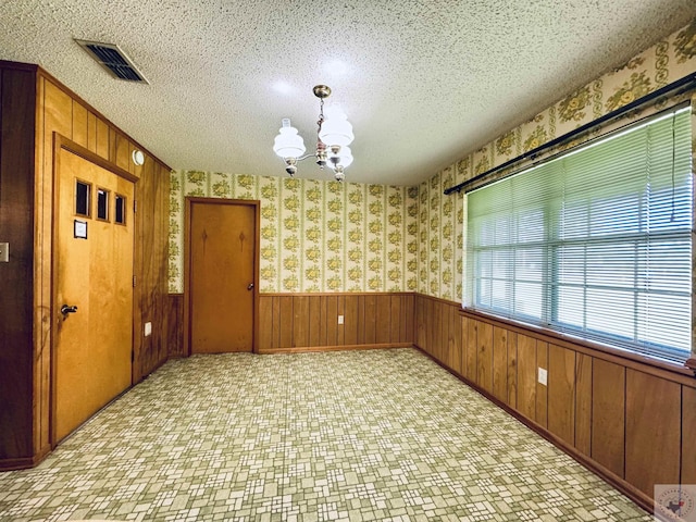 empty room with a textured ceiling, wood walls, and a chandelier