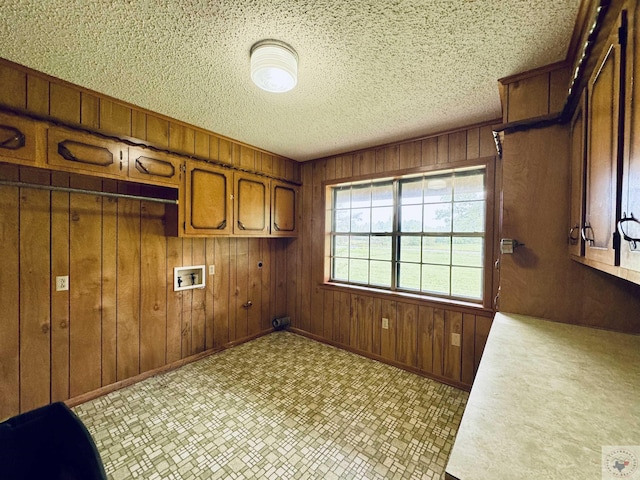 clothes washing area with washer hookup, cabinets, a textured ceiling, and wooden walls