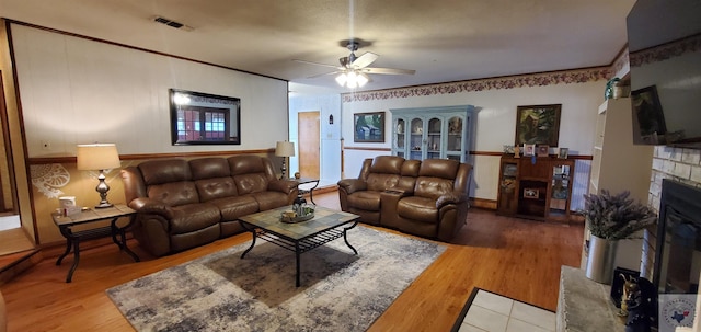 living room featuring ceiling fan, hardwood / wood-style floors, and a stone fireplace