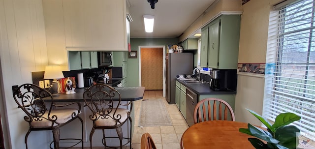 kitchen with a kitchen breakfast bar, green cabinets, sink, light tile patterned floors, and stainless steel refrigerator