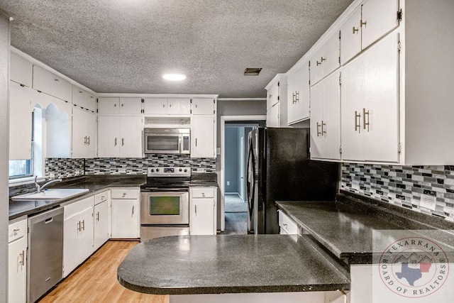 kitchen with white cabinets, dark countertops, appliances with stainless steel finishes, light wood-type flooring, and a sink