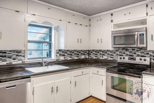 kitchen with appliances with stainless steel finishes, dark countertops, a sink, and white cabinets