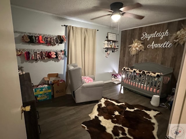 bedroom featuring a textured ceiling, wooden walls, a nursery area, dark hardwood / wood-style flooring, and ceiling fan