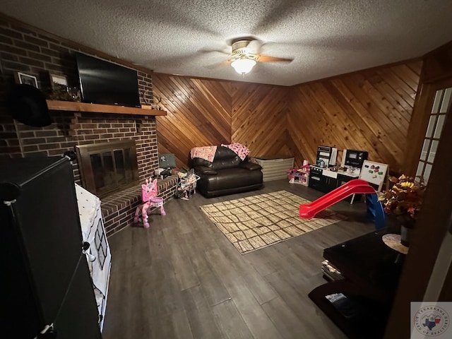 rec room featuring wood-type flooring, ceiling fan, a brick fireplace, a textured ceiling, and wooden walls