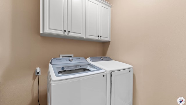 clothes washing area with separate washer and dryer and cabinet space