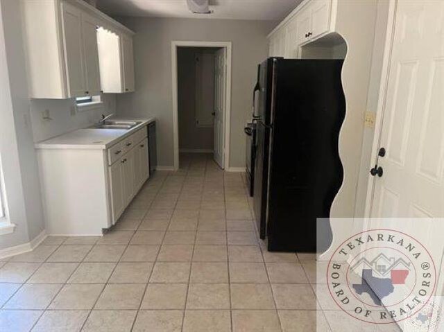 kitchen featuring sink, white cabinets, black fridge, and light tile patterned floors