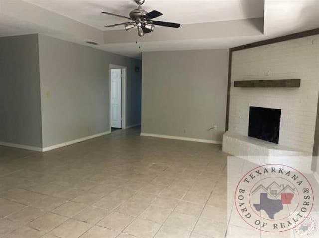 unfurnished living room with ceiling fan, a raised ceiling, and a fireplace