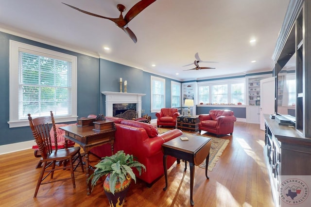 living room with ceiling fan, a high end fireplace, ornamental molding, and light hardwood / wood-style floors