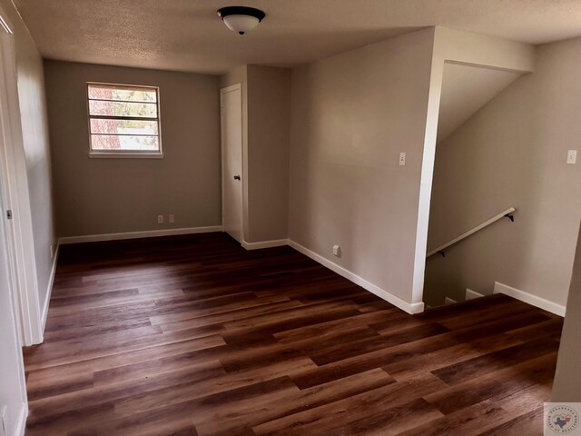 empty room with baseboards, dark wood-type flooring, and a textured ceiling