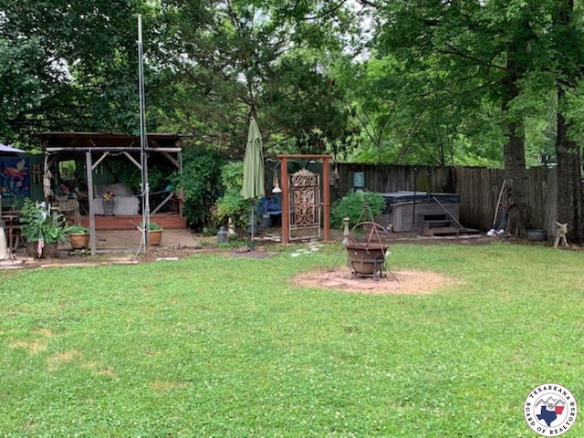 view of yard featuring a fire pit, a hot tub, and fence