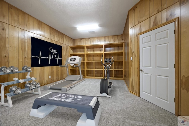 workout room featuring light colored carpet, a textured ceiling, and wooden walls