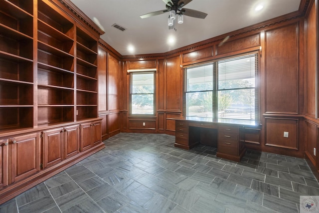 unfurnished office with ceiling fan, wooden walls, visible vents, and a decorative wall