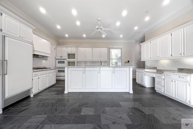 kitchen with ornamental molding, white appliances, white cabinetry, and a center island with sink