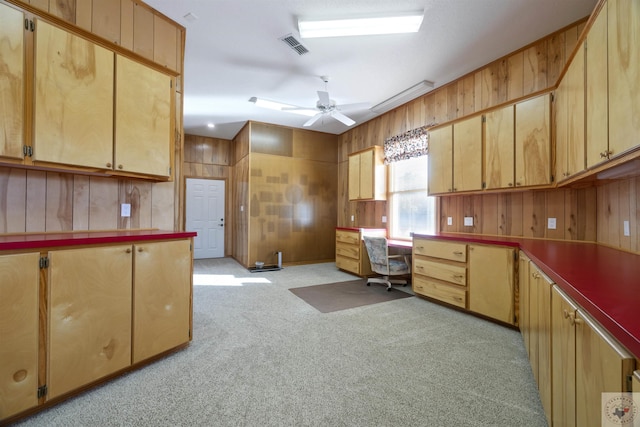 kitchen with light carpet, wood walls, ceiling fan, and built in desk