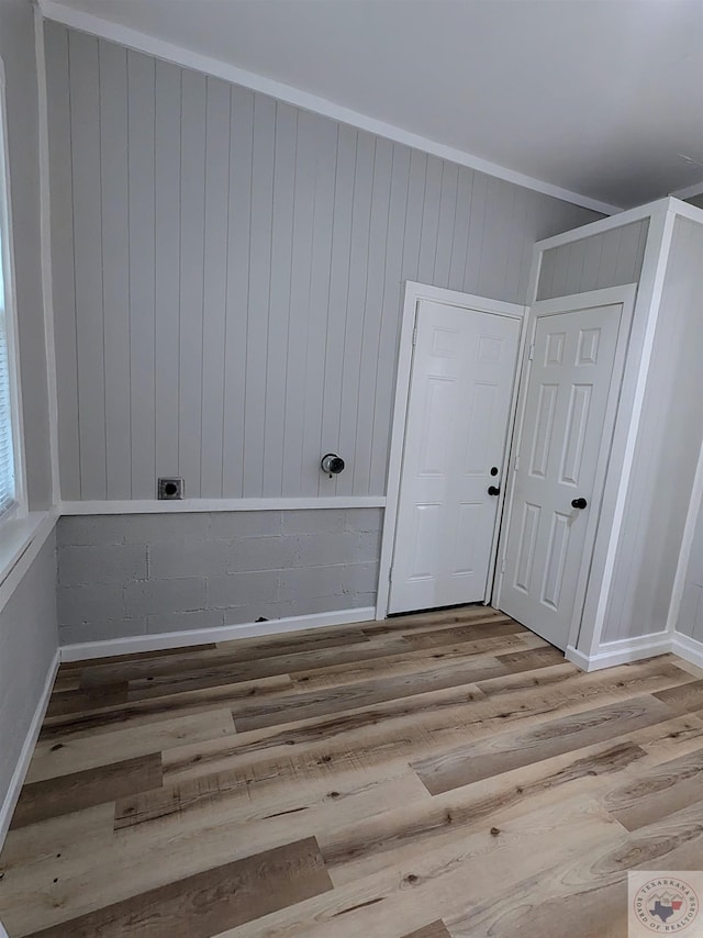 empty room with crown molding, wooden walls, and light hardwood / wood-style floors