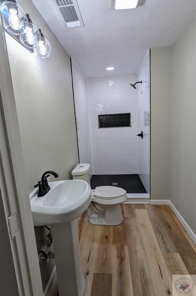 bathroom with a tile shower, hardwood / wood-style floors, toilet, and a textured ceiling