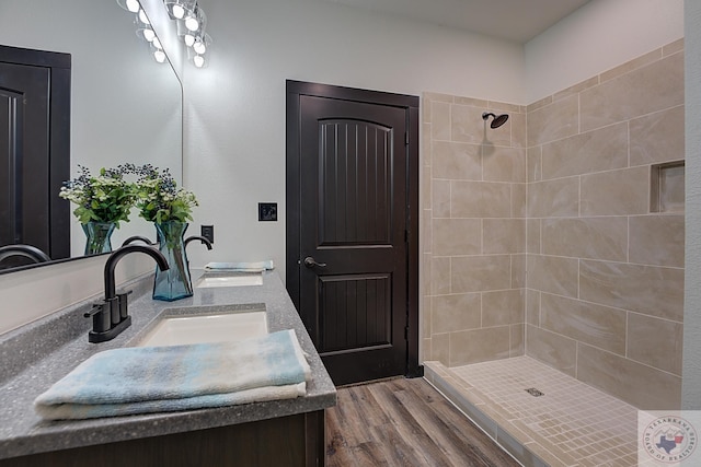 bathroom with wood-type flooring, a tile shower, and vanity