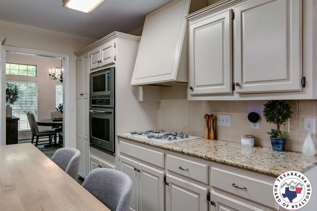 kitchen featuring stainless steel appliances, a chandelier, backsplash, crown molding, and premium range hood