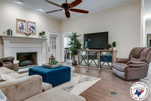 living area featuring ceiling fan, crown molding, wood finished floors, and a fireplace