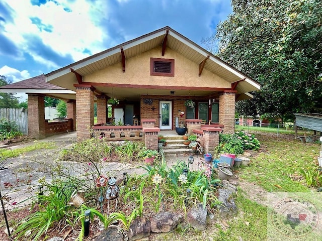 view of front of property featuring covered porch, brick siding, fence, and stucco siding