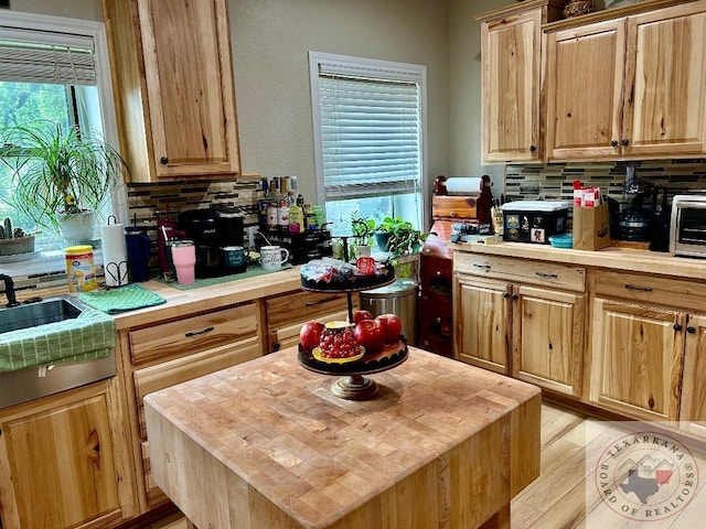 kitchen featuring a center island, light wood-style flooring, decorative backsplash, a sink, and butcher block countertops