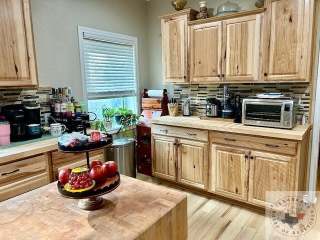 kitchen with light brown cabinetry, light wood finished floors, backsplash, and a toaster