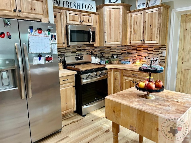 kitchen featuring light wood finished floors, appliances with stainless steel finishes, backsplash, and light brown cabinetry