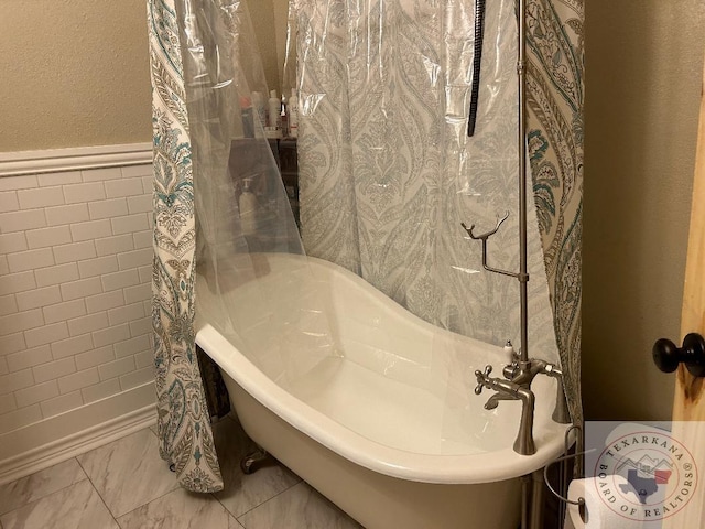 full bath with marble finish floor, wainscoting, a soaking tub, and tile walls