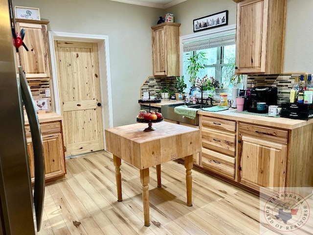 kitchen with light brown cabinets, a sink, light countertops, light wood finished floors, and tasteful backsplash