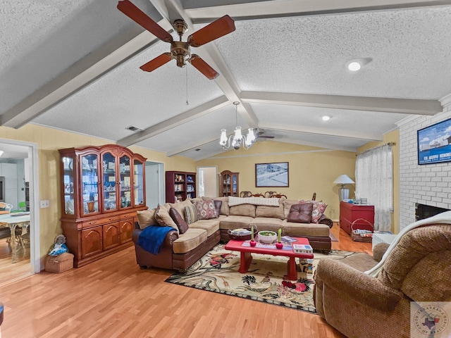 living room featuring ceiling fan with notable chandelier, a textured ceiling, a fireplace, lofted ceiling with beams, and light wood-type flooring