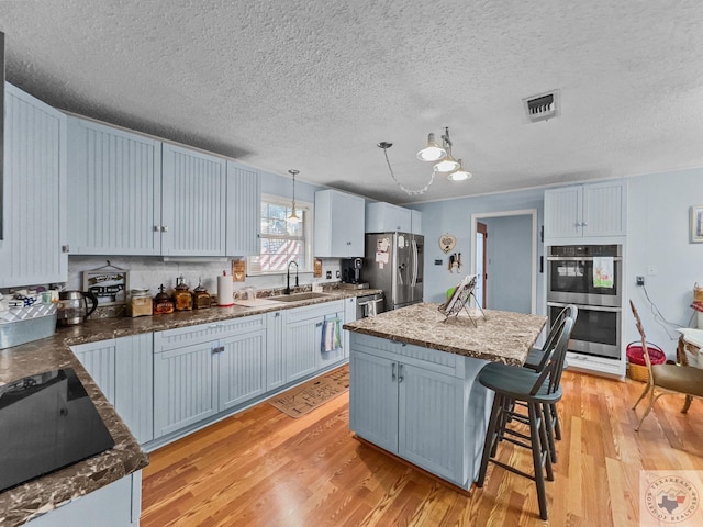 kitchen with pendant lighting, a kitchen island, stainless steel appliances, light hardwood / wood-style floors, and sink