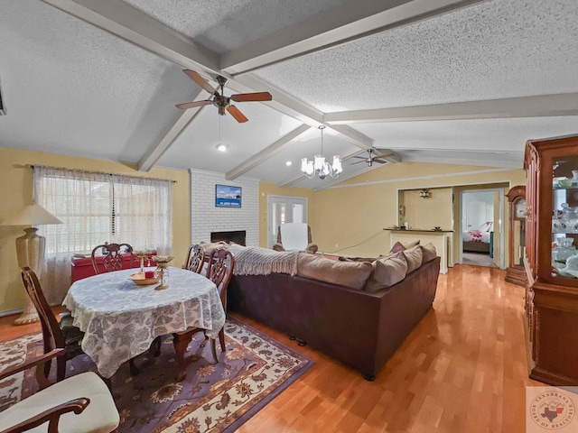 living room featuring hardwood / wood-style flooring, a fireplace, ceiling fan with notable chandelier, a textured ceiling, and vaulted ceiling with beams