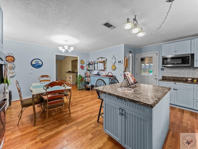 kitchen with a center island, a textured ceiling, tasteful backsplash, hanging light fixtures, and light hardwood / wood-style flooring