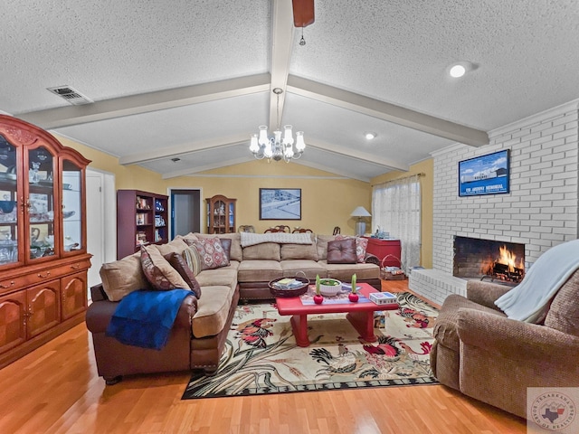 living room with wood-type flooring, a brick fireplace, a textured ceiling, vaulted ceiling with beams, and an inviting chandelier