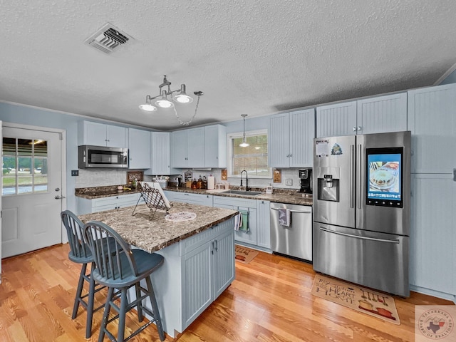 kitchen featuring appliances with stainless steel finishes, hanging light fixtures, sink, a kitchen island, and light hardwood / wood-style flooring