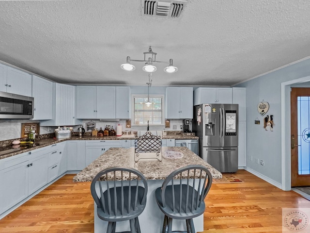 kitchen featuring light hardwood / wood-style floors, hanging light fixtures, white cabinets, a kitchen island, and stainless steel appliances