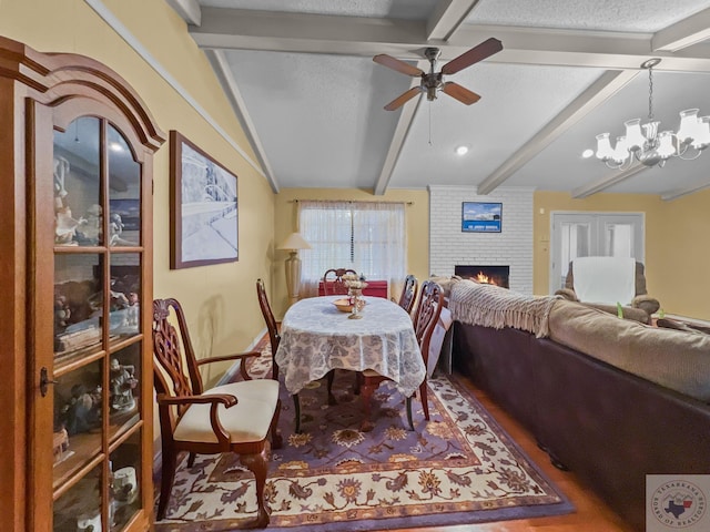 dining area with a fireplace, ceiling fan with notable chandelier, lofted ceiling with beams, and a textured ceiling