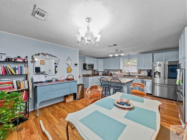 dining area featuring a textured ceiling, sink, a notable chandelier, light wood-type flooring, and crown molding