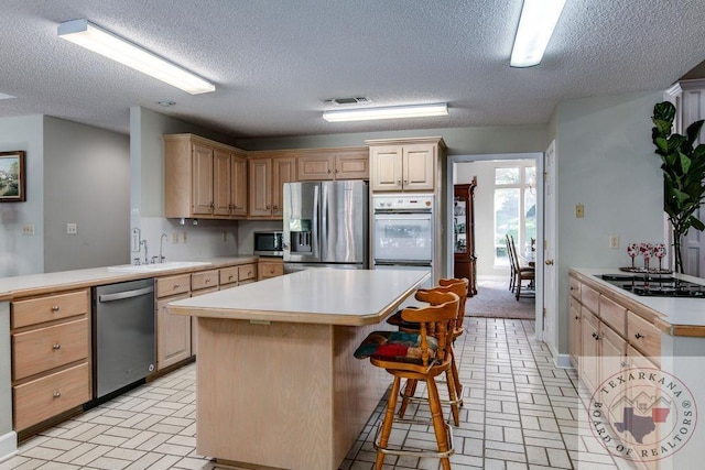 kitchen with a textured ceiling, a center island, stainless steel appliances, light brown cabinetry, and sink