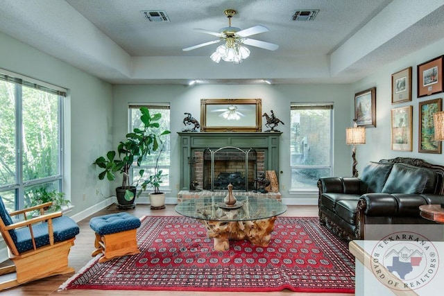 living room featuring hardwood / wood-style floors, a textured ceiling, a fireplace, ceiling fan, and a tray ceiling