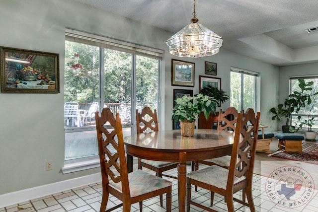 dining room featuring a textured ceiling, a tray ceiling, a notable chandelier, and a healthy amount of sunlight