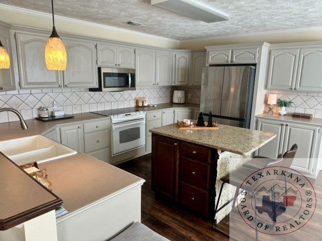 kitchen with pendant lighting, sink, ornamental molding, decorative backsplash, and stainless steel appliances