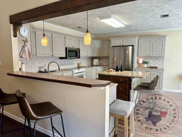 kitchen with kitchen peninsula, appliances with stainless steel finishes, sink, decorative light fixtures, and a kitchen bar