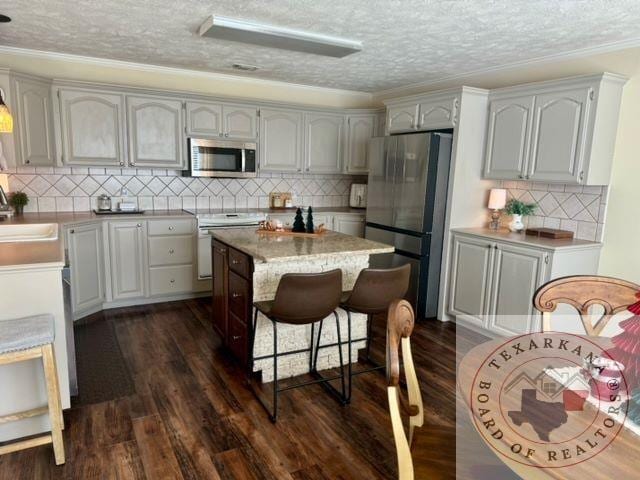 kitchen with appliances with stainless steel finishes, sink, dark wood-type flooring, a textured ceiling, and a kitchen island