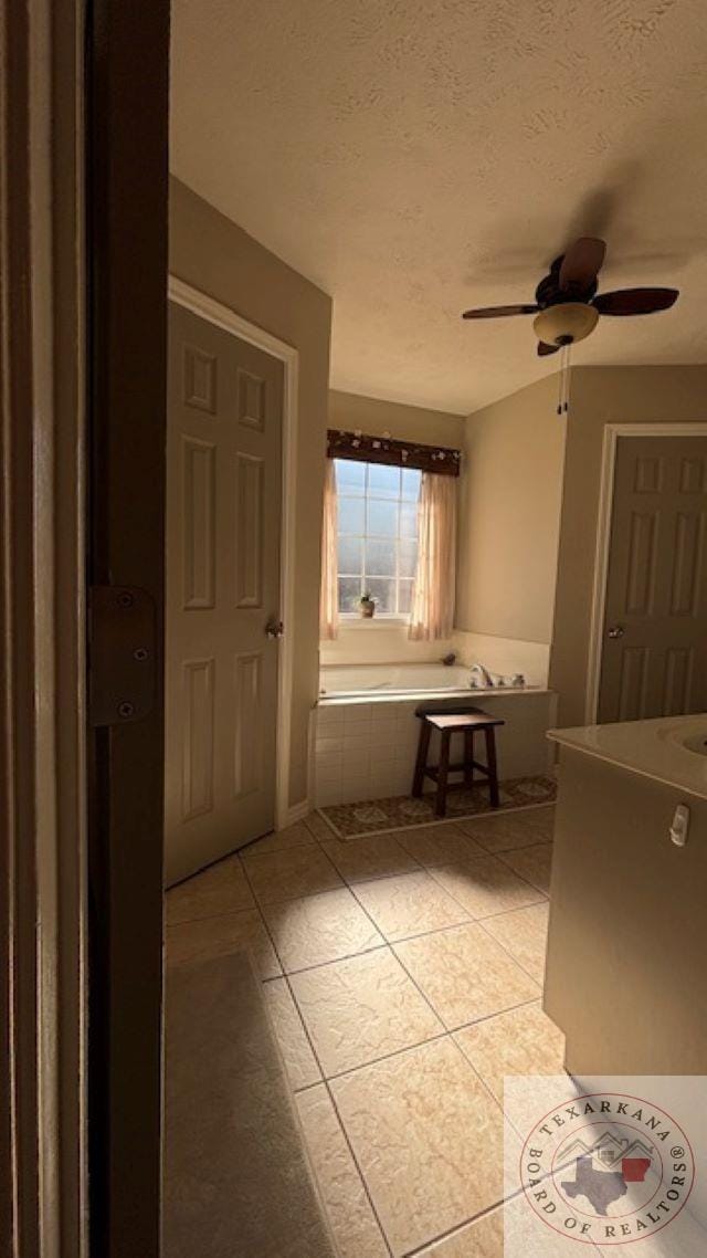 bathroom featuring ceiling fan, a textured ceiling, a relaxing tiled tub, and tile patterned flooring