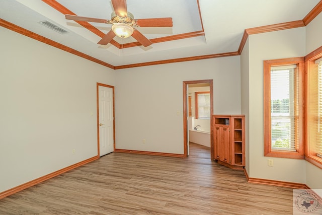 empty room featuring a raised ceiling, light hardwood / wood-style flooring, crown molding, and a healthy amount of sunlight