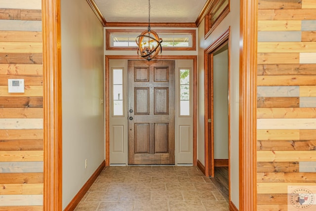 entrance foyer with a notable chandelier, ornamental molding, wooden walls, and a textured ceiling