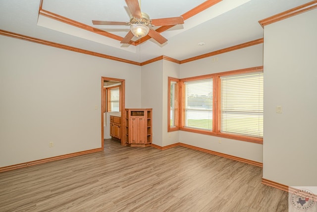 empty room with crown molding, a healthy amount of sunlight, light hardwood / wood-style flooring, and a tray ceiling