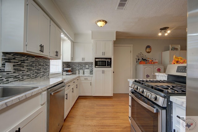 kitchen featuring appliances with stainless steel finishes, white cabinetry, tasteful backsplash, ornamental molding, and light wood-type flooring