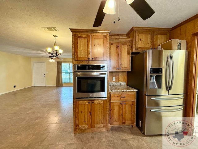 kitchen with stainless steel appliances, ceiling fan with notable chandelier, light stone counters, and a textured ceiling